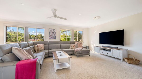 A modern living room with a sectional sofa, a flat-screen TV, and a ceiling fan.