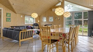 Una habitación amplia con techo de madera, una mesa de comedor con sillas, un sofá y un ventanal con vistas al exterior.