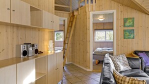 Interior acogedor de una cabaña con paredes de madera, una cama en el entrepiso, un sofá y una cocina con electrodomésticos.