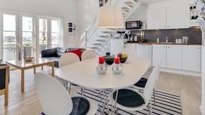 A modern kitchen with white cabinets, a microwave, and a coffee machine. There is a dining area with a white table and chairs, and a staircase leading to an upper level. - "Idunn" - 100m to the fjord by Interhome (Vestervig)