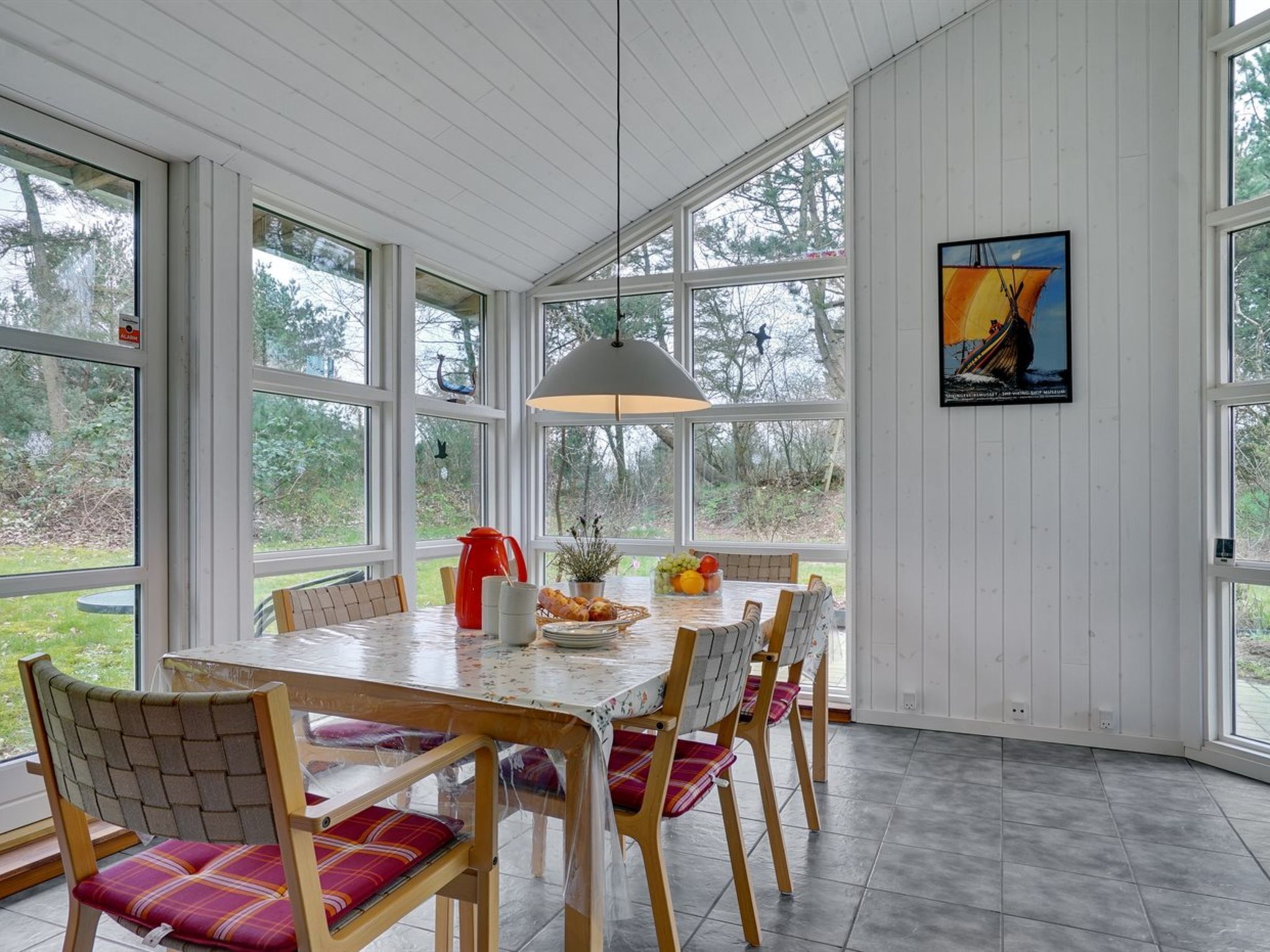 A dining area with a table set for six, surrounded by wooden chairs with plaid cushions.