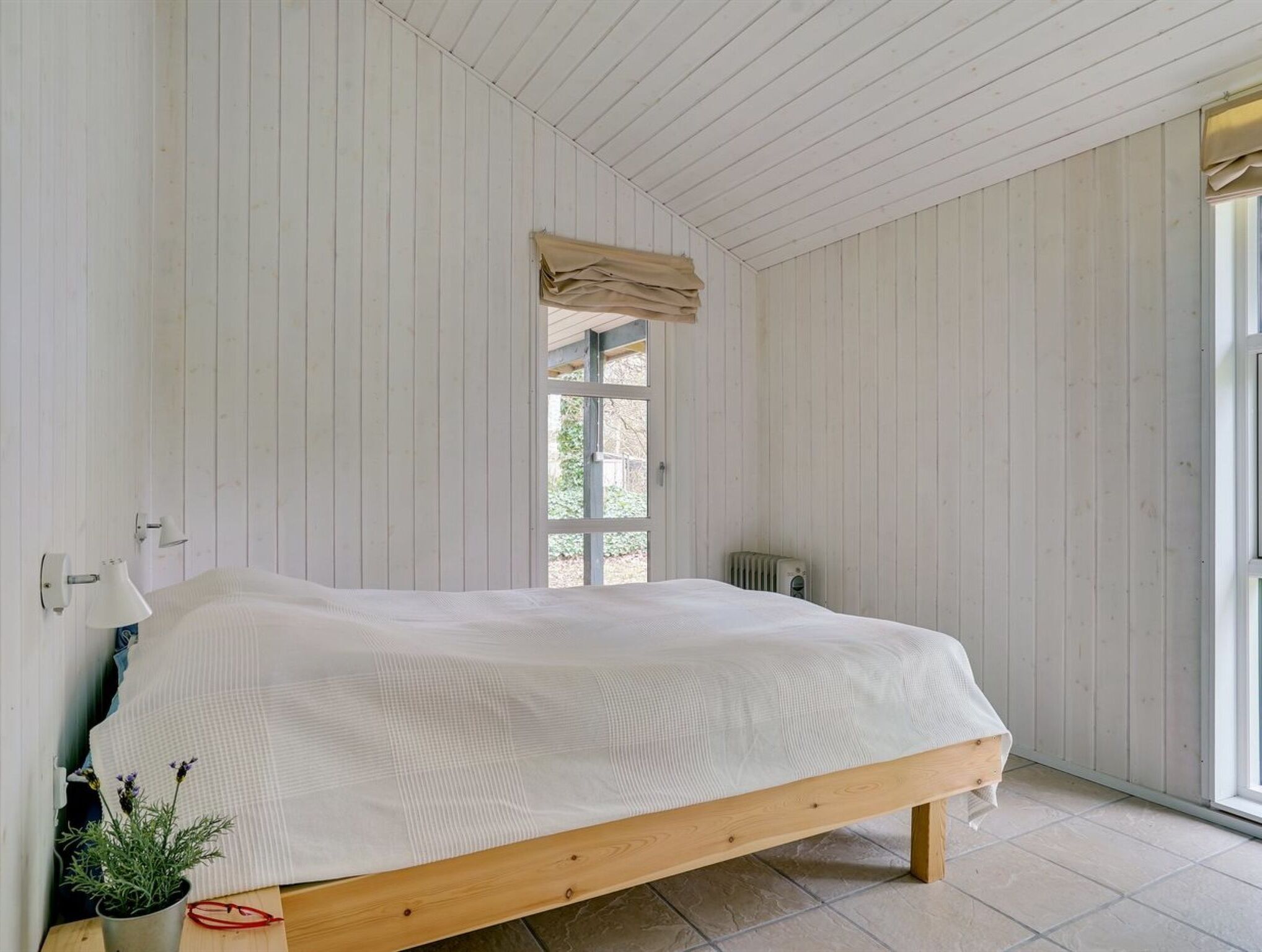 A bedroom with a wooden bed, a window with a view, and a radiator.