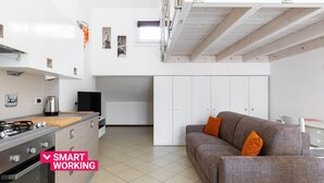 Eine moderne Küche mit Gasherd, weißen Schränken und einem grauen Sofa mit orangefarbenen Kissen.