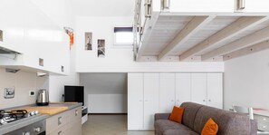 Eine moderne Küche mit Gasherd, weißen Schränken und einem grauen Sofa mit orangefarbenen Kissen.