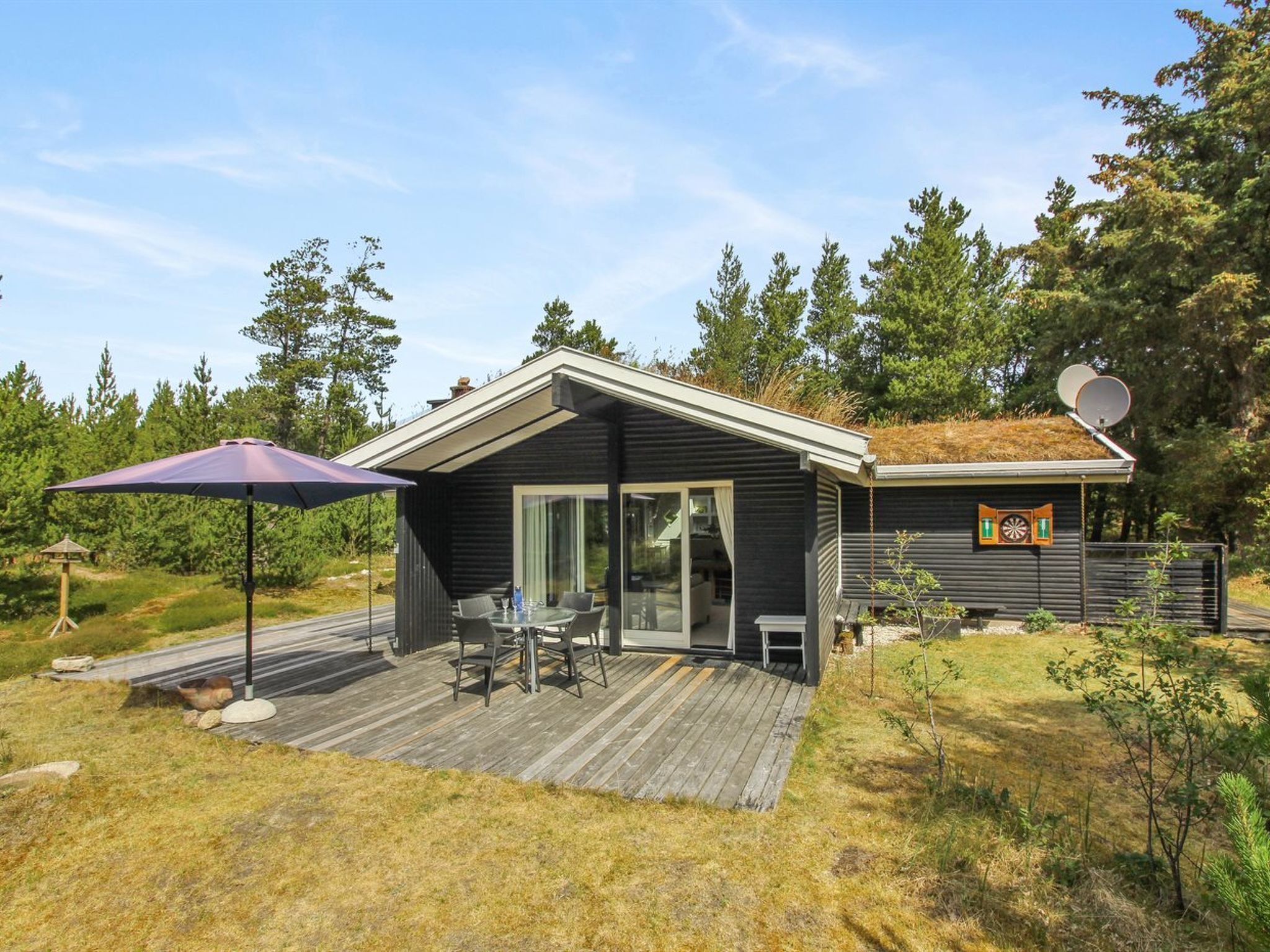 Een moderne blokhut met terras, een zonnescherm en een schotelantenne.