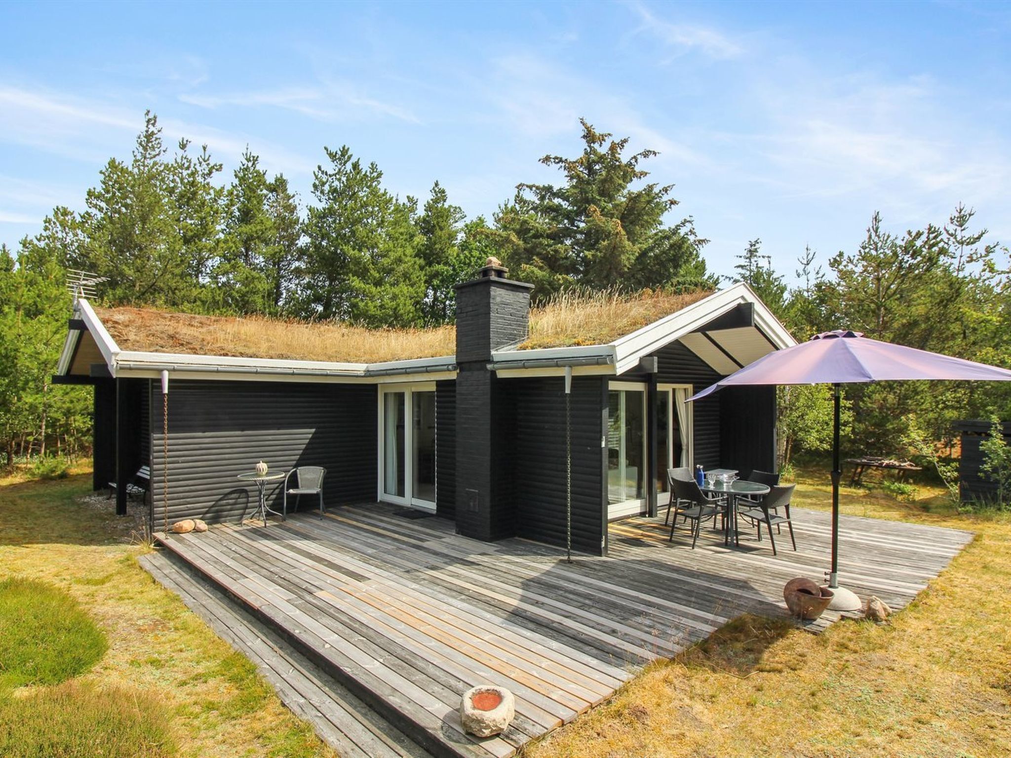 A modern cabin with a sloped roof, a deck, and a patio area with outdoor furniture.
