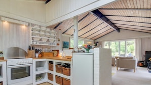 A modern kitchen with white cabinetry, a stove, and a large island. There are wicker baskets on the lower shelves and a large window providing natural light. - "Heike" - 1.3km from the sea by Interhome (Blokhus)