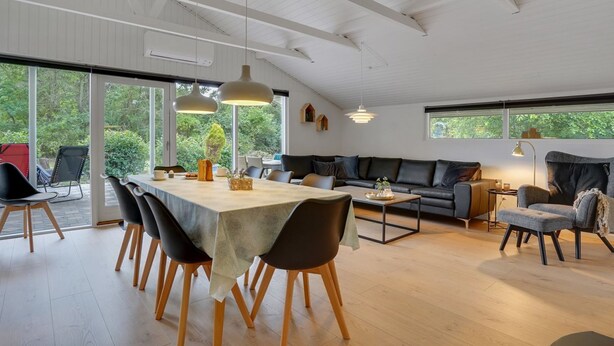 Een ruime woonkamer met een eettafel, banken en een groot raam met uitzicht op groen.