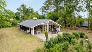 Een gelijkvloers huis met een overdekte veranda, een gazon en omliggende bomen.