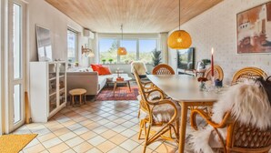 Een moderne woonkamer met een eetgedeelte, houten plafond, grote ramen en uitzicht op de omgeving.