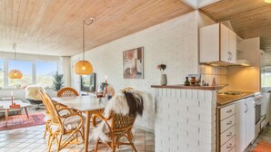 Een moderne keuken met witte bakstenen muren, een houten plafond en een eetgedeelte met rieten stoelen en een witte tafel.