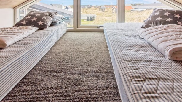 Een slaapkamer met twee bedden, een vloerbedekking en een groot raam met uitzicht op huizen en een grasveld.