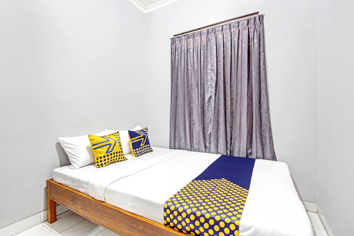 Un dormitorio con una cama de madera, ropa de cama blanca, una colcha celeste y amarilla con lunares y cortinas grises.
