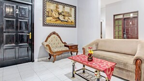 A room with a beige sofa, a wooden chair, a table with a red tablecloth, and a framed picture on the wall. - OYO Life 92575 Zazi Homestay (Depok)