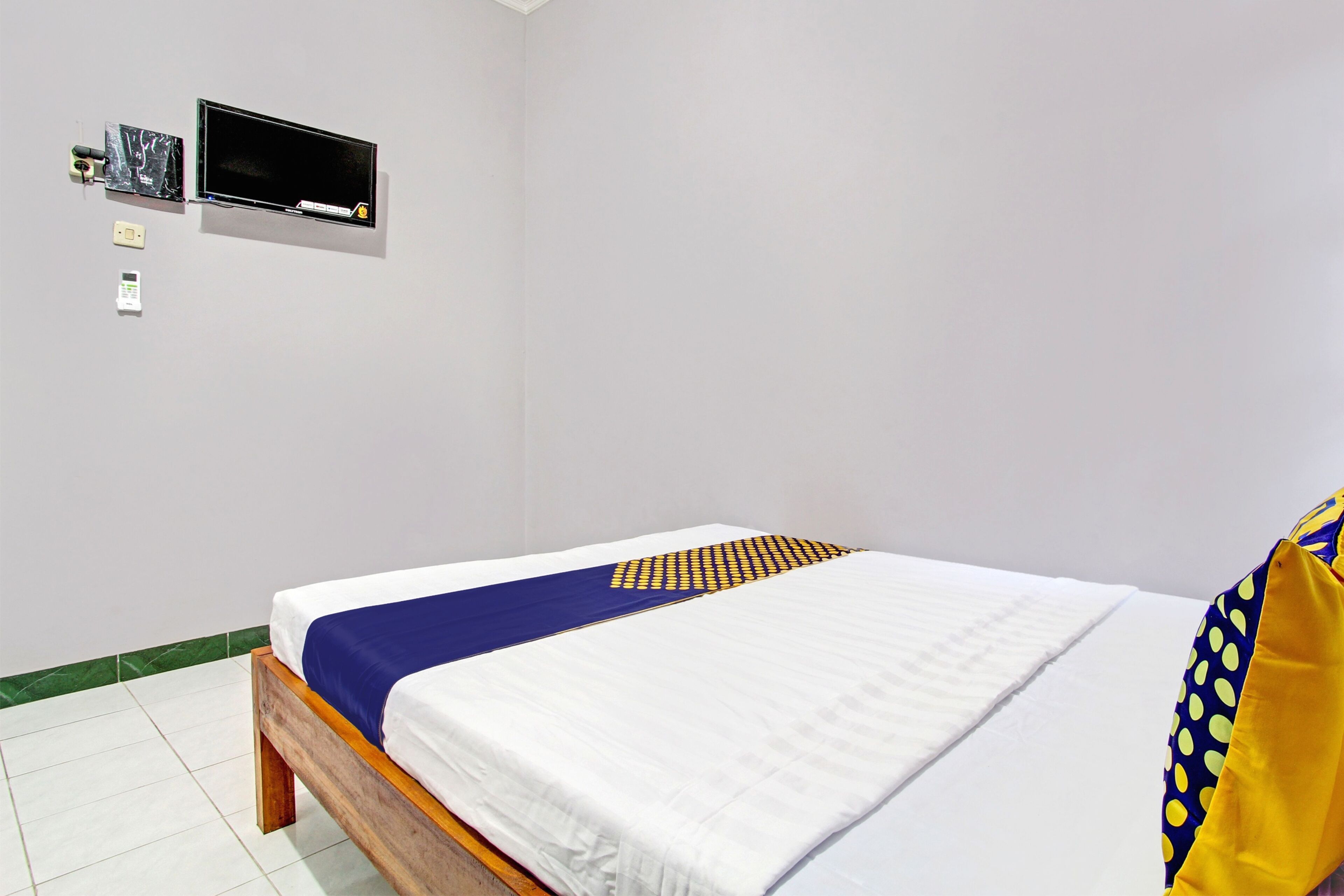 A neatly made bed with a white and blue bedspread, a wooden headboard, and a television mounted on the wall.