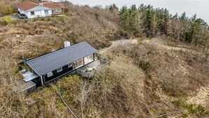 Una casa moderna con techo metálico, rodeada de un bosque denso y con vista a una gran masa de agua.