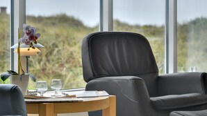 Una camera moderna con una grande finestra, una poltrona in pelle nera, un comodino in legno con una lampada e un bicchiere d'acqua.