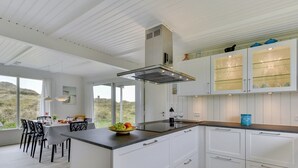 Una cucina moderna con mobili bianchi, un'isola centrale e un'area pranzo con vista sull'esterno.