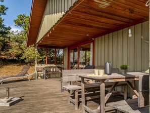 Una terraza de madera con mobiliario exterior, incluyendo una mesa y sillas, y una hamaca.