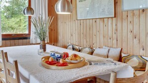 Un intérieur en bois avec une table à manger dressée pour le petit-déjeuner, un canapé avec des coussins et une carte encadrée accrochée au mur.