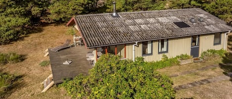 Una casa de una sola planta con techo inclinado, un pequeño porche con una silla y una chimenea visible.