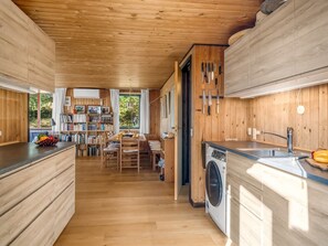 Une cuisine compacte dotée de meubles en bois, d’un lave-linge encastré et d’un coin repas avec une table et des chaises.