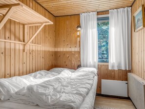A wooden room with a bed, a window with curtains, and a radiator.
