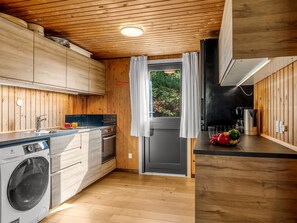 A compact kitchen with wooden cabinets, a built-in washing machine, and a small dining area with a fruit bowl.
