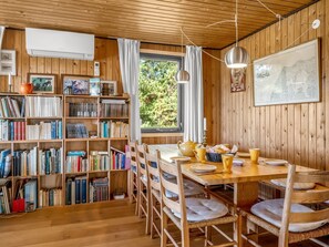 Interior acogedor de una cabaña, con paredes de madera, una mesa de comedor preparada para cuatro personas y una estantería llena de libros.