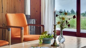 Un intérieur en bois avec une chaise, une table ornée d’un vase de fleurs, une bougie et un bol de raisins.