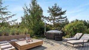 A wooden deck with outdoor seating, a hot tub, and surrounding greenery.