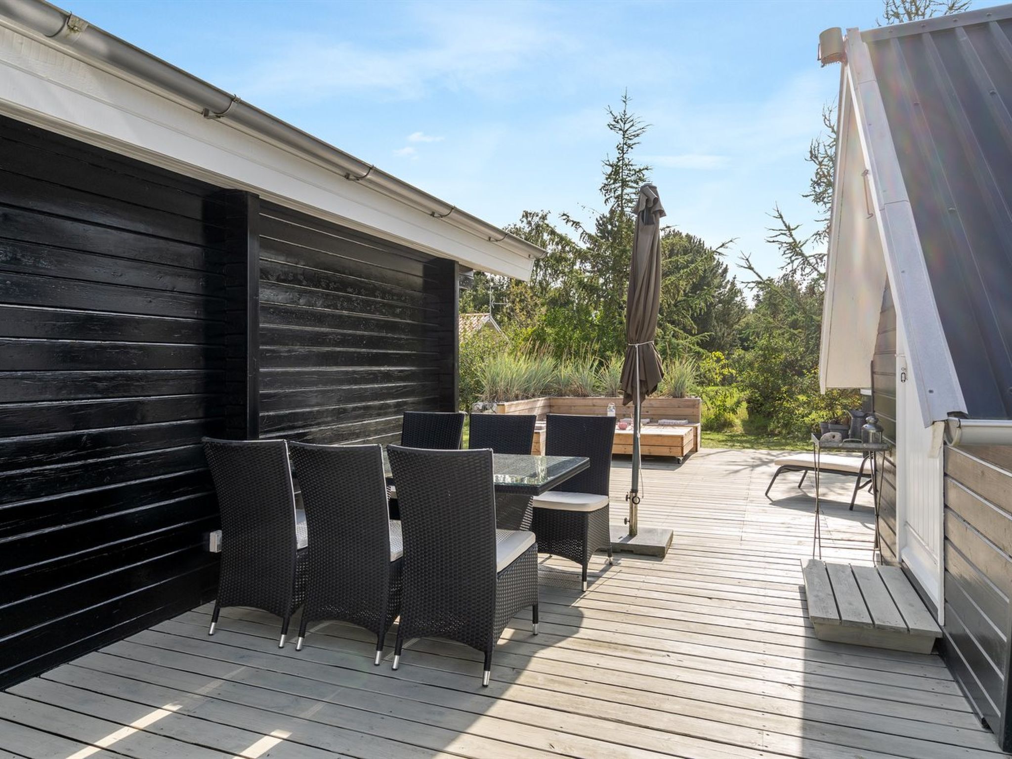 An outdoor patio with a black wall, wicker furniture, and a wooden deck.