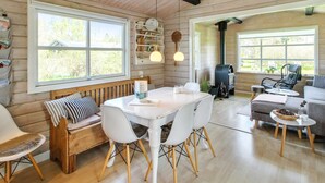 A cozy cabin interior with a wooden interior, a dining area with a white table and chairs, a sofa, and a fireplace.