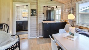 A cozy cabin interior with a wooden ceiling, a kitchen area, a dining table, and a window with a view.