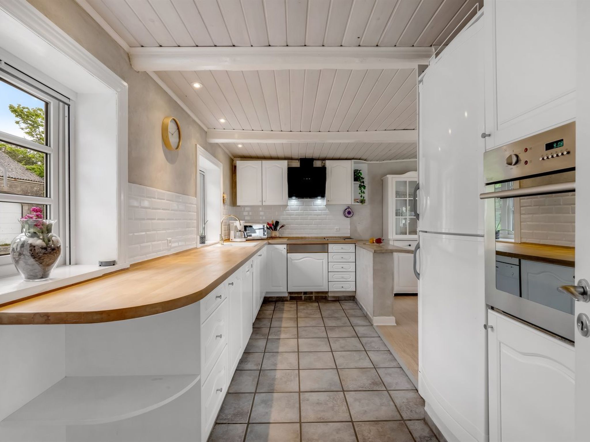 Une cuisine moderne avec des meubles blancs, un plan de travail en bois et un sol carrelé.