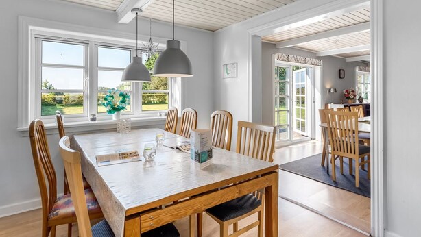 A dining area with a wooden table and chairs, pendant lights, and large windows offering a view of the outdoors. - "Merrit" - 4.6km to the fjord by Interhome (Hemmet)