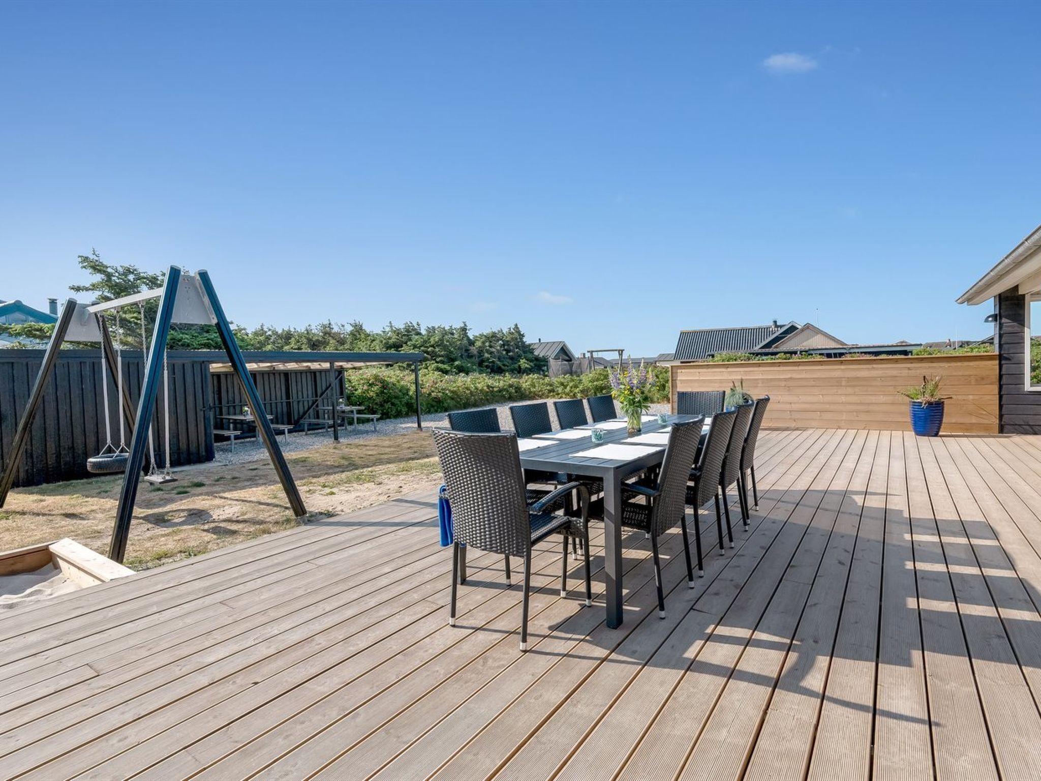 Una terraza de madera con una mesa y sillas para comer, un columpio y una zona de estar cubierta.