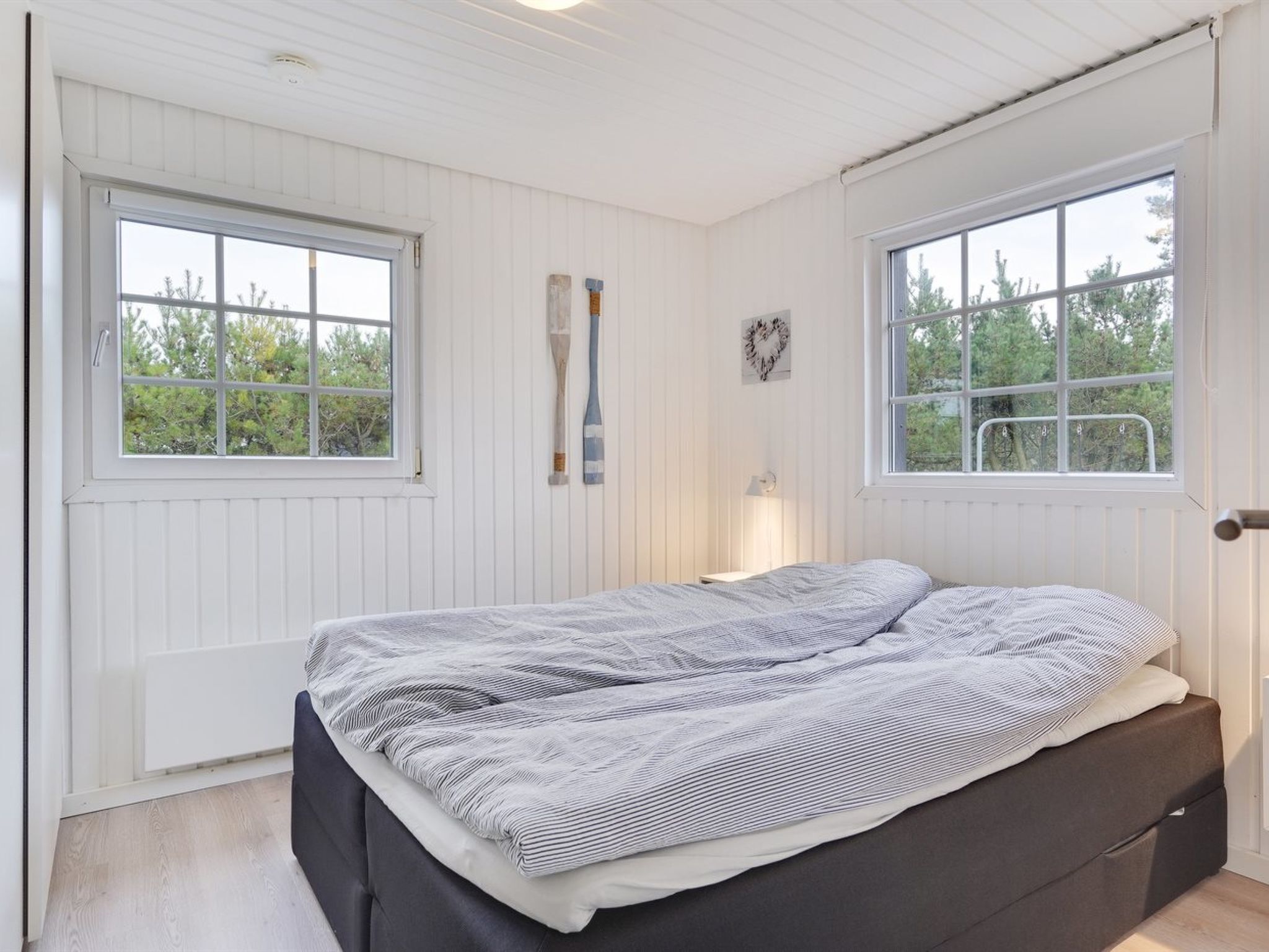 A bedroom with a bed, two windows, a radiator, and a wall-mounted lamp.