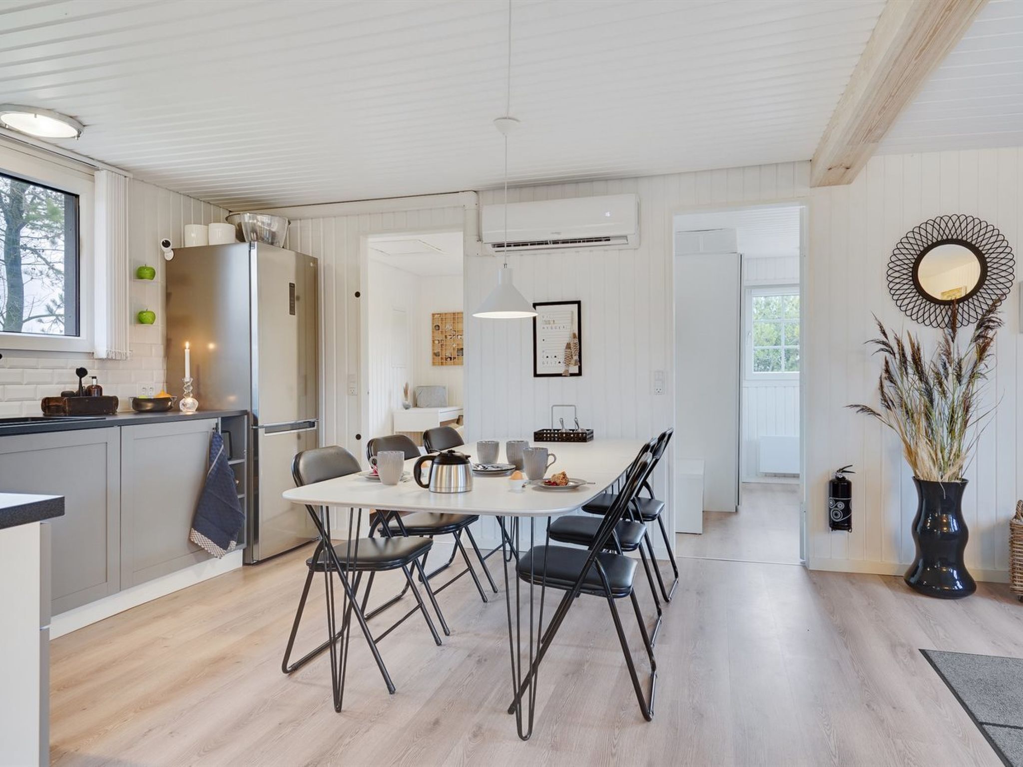 Een moderne keuken met een eethoek, met een witte tafel en zwarte stoelen, een groot raam en een decoratieve spiegel.