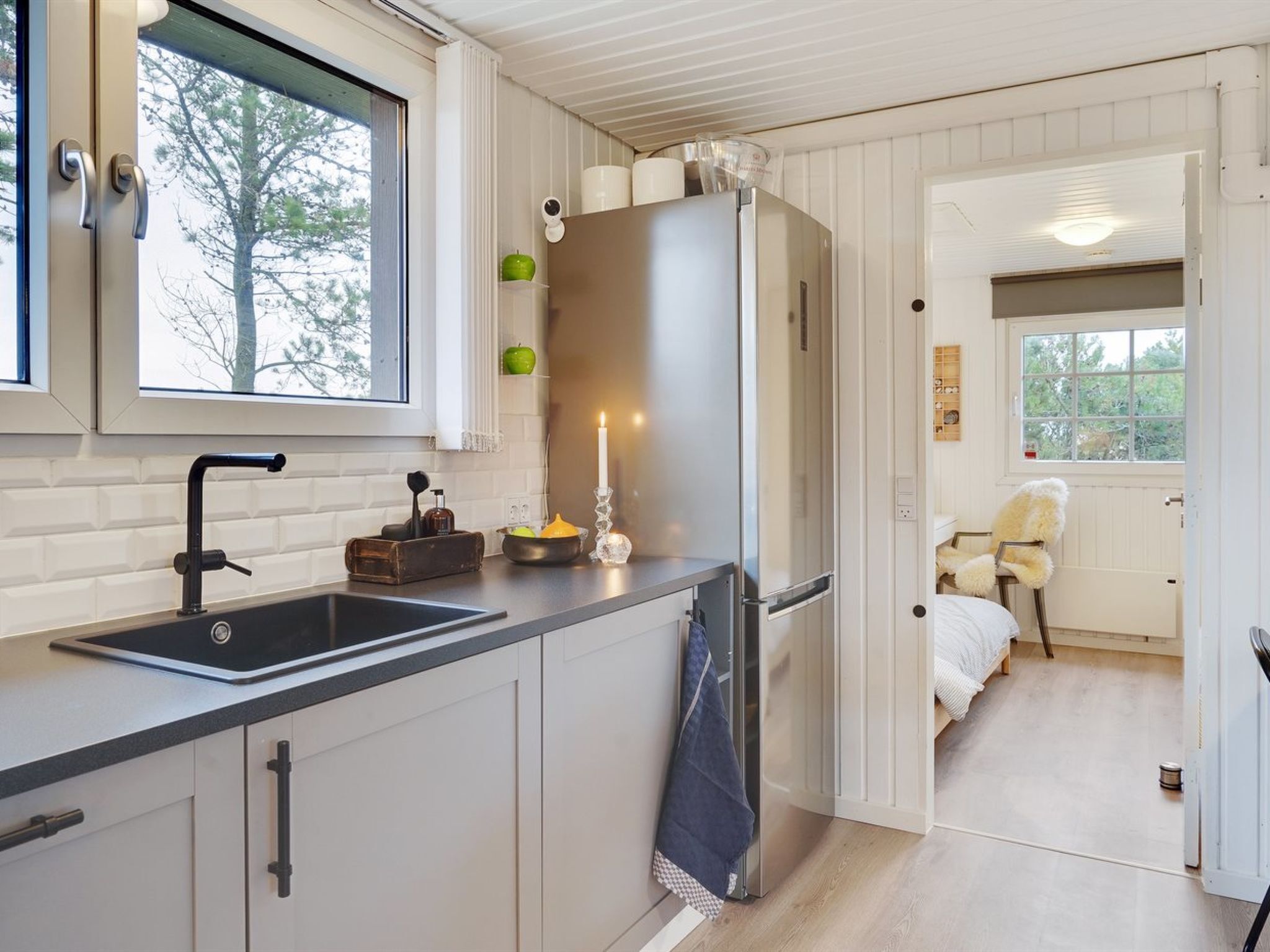 Een moderne keuken met een roestvrijstalen koelkast, een zwarte kraan en een raam met uitzicht op bomen.