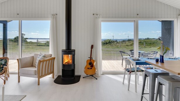A modern living room with a wood-burning stove, a guitar, and a dining area with a view of wind turbines. - "Rickmer" - 200m from the sea by Interhome (Ebeltoft)