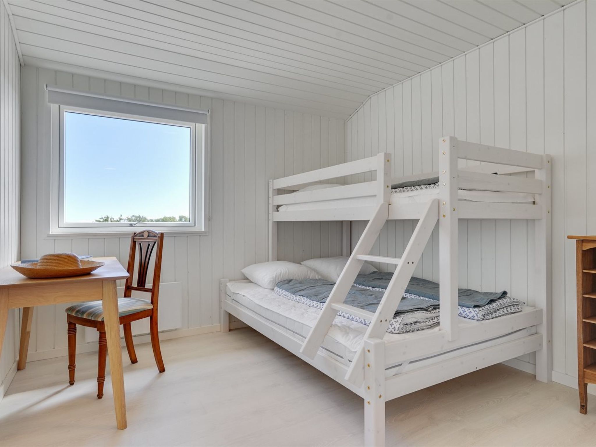 Une chambre avec un lit superposé, un bureau en bois, une chaise et une fenêtre.
