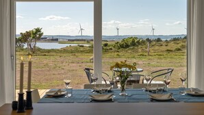 A dining area with a table set for four, overlooking a landscape with wind turbines and a body of water. - "Rickmer" - 200m from the sea by Interhome (Ebeltoft)