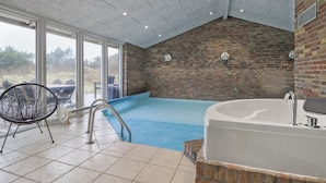 A modern indoor swimming pool with a brick wall, a large bathtub, and a chair.