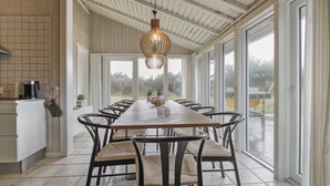 A spacious kitchen with a long wooden table and chairs, large windows, and a hanging light fixture.