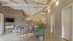 A spacious living area with a brick wall, a grey sofa, a wicker chair, and a potted plant.