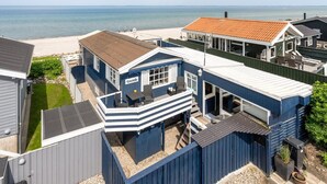 Una casa costera con balcón, vista al mar y una playa arenosa en el fondo.