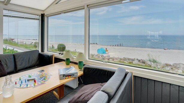 Una habitación con un ventanal grande con vistas a una playa, una mesa con un juego de mesa y un sofá.