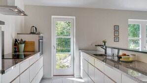 A modern kitchen with a central island, built-in appliances, and a view through a glass door. - "Kringfod" - 590m from the sea by Interhome (Hals)
