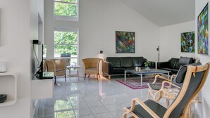 A spacious living room with a black leather sofa, wooden chairs, and a coffee table. Large windows allow natural light to fill the space. - "Kringfod" - 590m from the sea by Interhome (Hals)